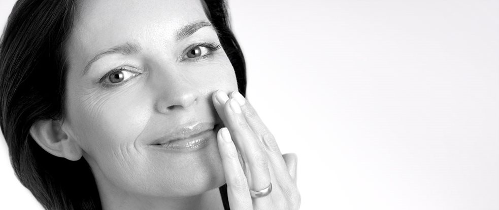 Middle-aged woman touching left cheek with hand.