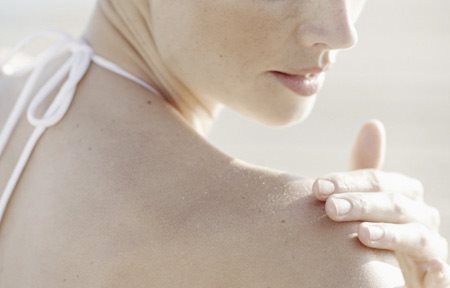 Woman is applying cream on her right shoulder.